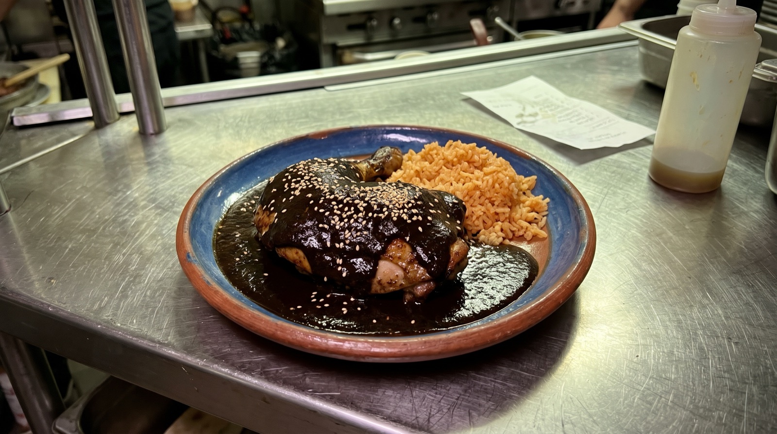 Phone photo of mole negro with chicken and red rice under green fluorescent light on a steel counter