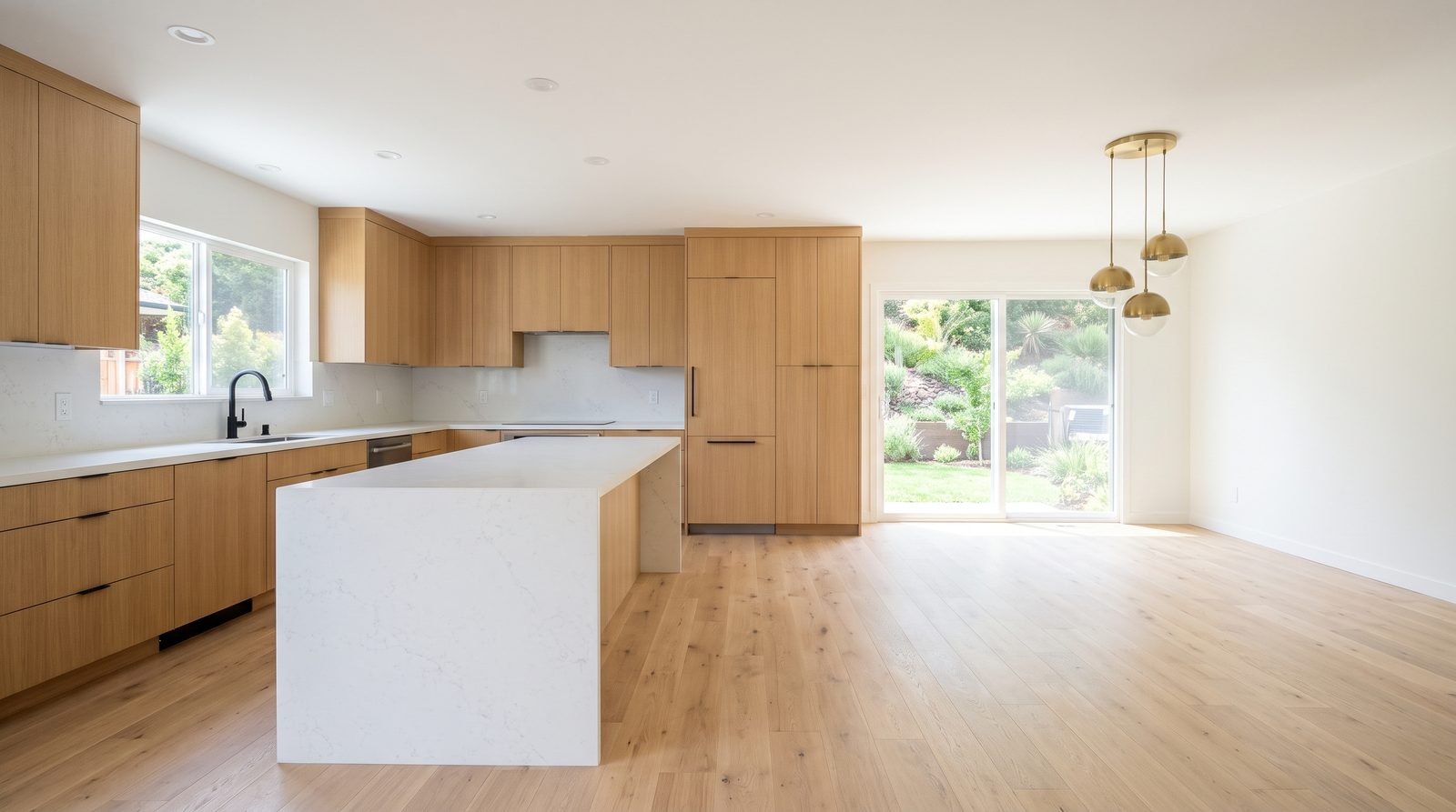 Kitchen with oak cabinets and a white waterfall island beside an empty dining area under brass pendant lights