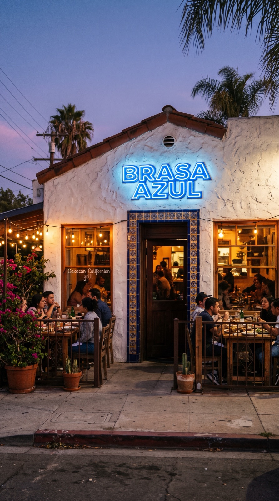 A white-plastered restaurant with blue tiles, string lights and a blue neon sign reading BRASA AZUL at dusk