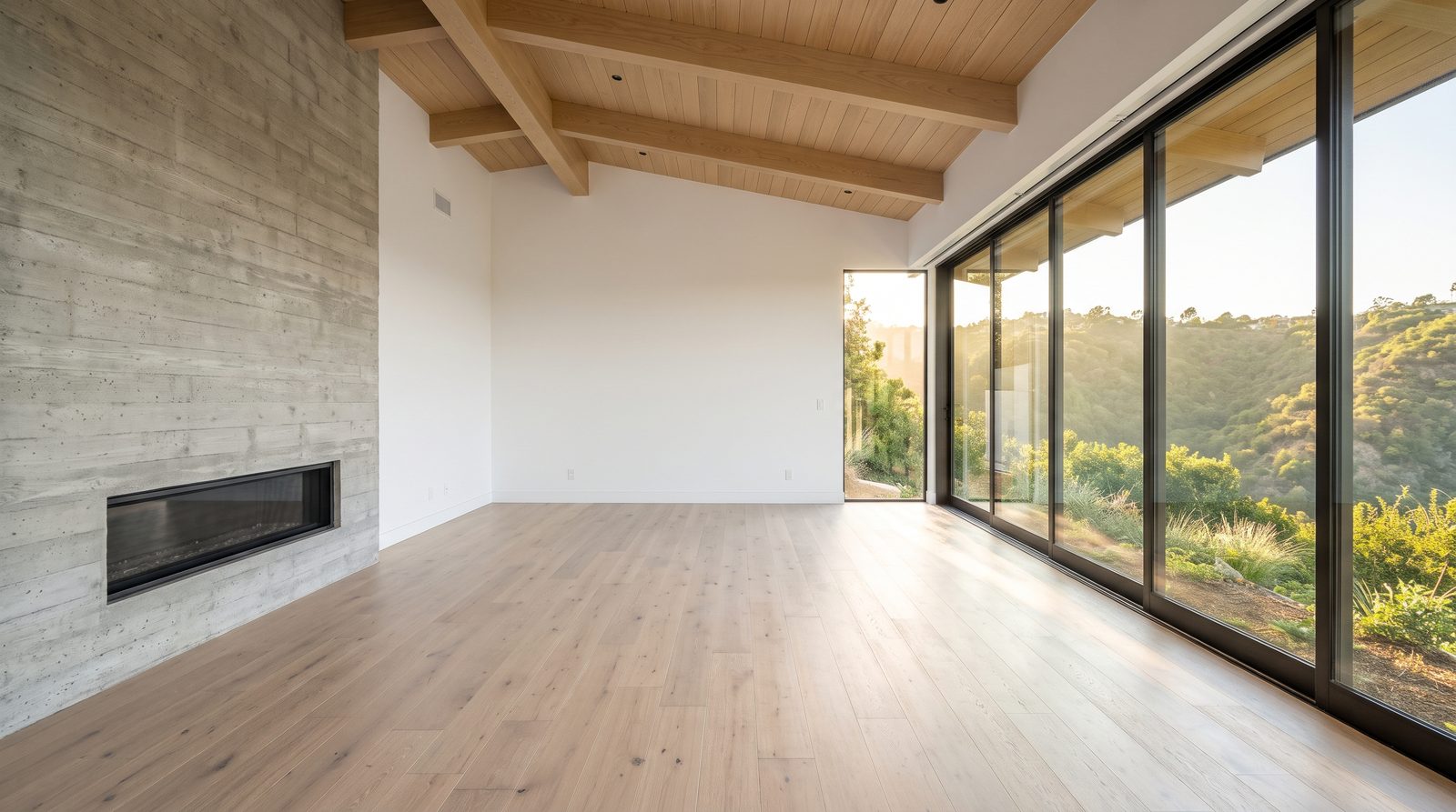 Empty living room with white oak floors, a concrete fireplace wall, exposed beams and a glass wall over a canyon